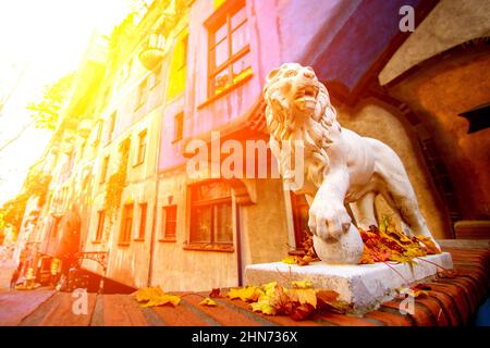 Eine schöne Skulptur eines weißen Löwen steht mit einer Pfote auf einem Ball, blickt zur Seite und knurrt vor dem Hintergrund einer schönen alten Architektur Stockfoto