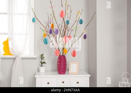 Vase mit Ästen und Osterdekor auf Tisch neben heller Wand Stockfoto