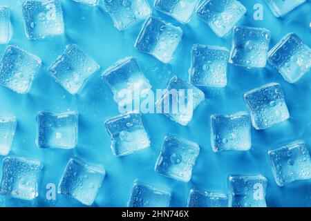 Viele frostige und erfrischende Eiswürfel mit Tropfen auf blauem Hintergrund. Erfrischende Getränke bei heißem Wetter Stockfoto