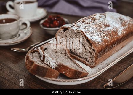 Frisch gebackener Kuchen auf dem Teller mit einer Tasse Tee und Kirschmarmelade aus der Nähe Stockfoto