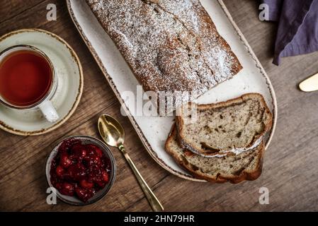 Frisch gebackener Kuchen auf dem Teller mit einer Tasse Tee und Kirschmarmelade von oben Stockfoto