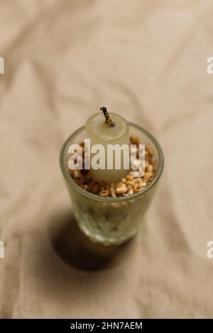 Weiße Kerze im Glas mit Weizenkorn auf Bastelkarton beige Hintergrund. Speichertag. Völkermord in der Ukraine. Holodomor. Holocaust. Vertikal Stockfoto