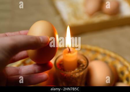 Hand hält Ei. Kerze mit Licht. Rustikaler Hintergrund. Ostereier, Pysankas. Sammlung von Eiern auf dem Hintergrund. Vorbereitung auf den Urlaub. Papier basteln Stockfoto