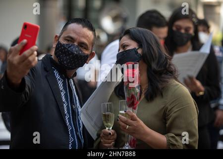 Veracruz, Mexiko. 14th. Februar 2022. Ein Paar mit Mundnasenbedeckung nimmt nach ihrer Hochzeit ein Selfie auf, das an einem vom Rathaus für mehrere Paare organisierten Termin stattfand. Mehr als 300 Paare hatten sich für diesen Termin angemeldet. Aufgrund der durch die Corona-Pandemie auferlegten Einschränkungen wurden jedoch nur 20 Paare zugelassen. Quelle: Felix Marquez/dpa/Alamy Live News Stockfoto