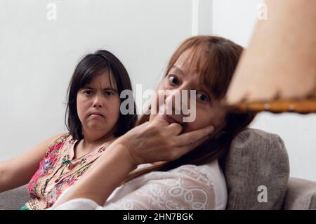 Porträt der Mutter und ihrer Tochter mit Down-Syndrom kaukasischen hispanischen Latein, sitzen auf dem Sofa im Wohnzimmer Blick auf die Kamera. Lifesty Stockfoto