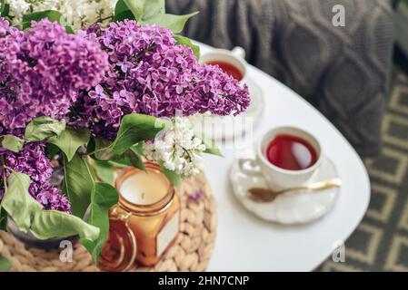 Bouquet von lila Flieder Blumen auf Couchtisch mit zwei Tassen Tee und Kerze in der häuslichen Einrichtung Stockfoto