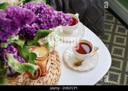 Bouquet von lila Flieder Blumen auf Couchtisch mit zwei Tassen Tee und Kerze in der häuslichen Einrichtung Stockfoto