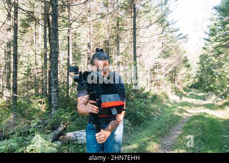 Professioneller Videograf, der eine DSLR-Kamera auf einem 3-Achsen-Gimbal-Stabilisator im Wald hält. Pro Equipment hilft, hochwertige Videos ohne Schütteln zu machen. Kameramann. Zeitlupe Stockfoto