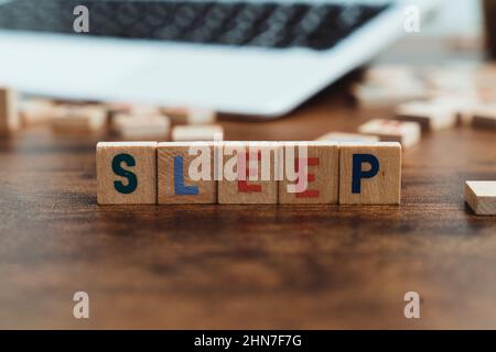 Schlaf Wort auf einem Holzblock geschrieben - Laptop-Tastatur im Hintergrund gesehen - Schlaflosigkeit Konzept. Hochwertige Fotos Stockfoto