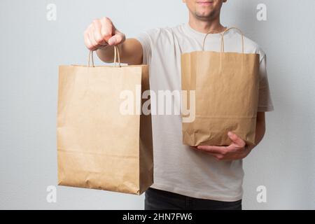 Lieferkonzept - schöner kaukasischer Liefermann, der eine Packtasche mit Lebensmitteln und Getränken aus dem Laden trägt. Isoliert auf grauem Studiohintergrund. Kopieren Stockfoto