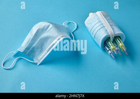 Insulin-Spritzenstifte mit medizinischen Masken auf blauem Hintergrund Stockfoto