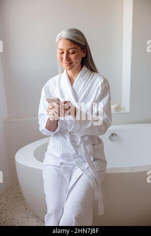 Vertikale Foto Frau sitzt auf dem Rand der Badewanne mit dem Smartphone Stockfoto