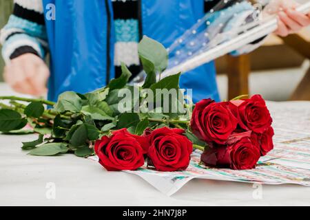 Frau Floristin macht Bouquet von roten Rosen. Kleines Unternehmen für Gärtner. Verkauf von Blumen im Blumenladen. Lifestyle. Stockfoto