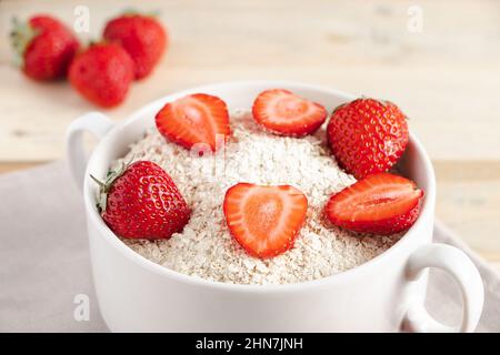 Haferflocken mit Erdbeeren in einer Schüssel auf Holzboden. Gesundes Frühstück. Konzept der Ernährung und glutenfreies Getreide. Stockfoto