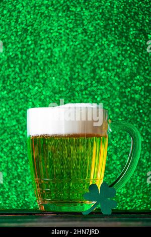 Becher helles Bier mit Schaum auf grünem Hintergrund. Traditionelles irisches Getränk. Wir feiern den St. Patrick's Day. Stockfoto