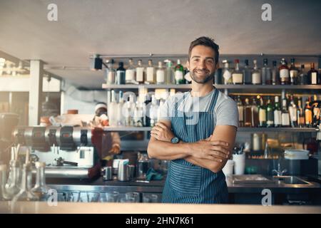 Es gibt einen Grund, warum meine Kunden immer wieder kommen. Porträt eines jungen Mannes, der hinter einer Theke arbeitet. Stockfoto