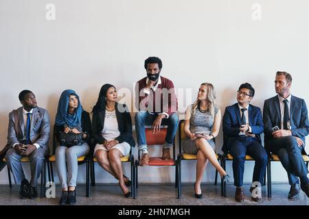 Sie werden von ihm eingeschüchtert. Aufnahme einer Gruppe von selbstbewussten Geschäftsleuten, die auf ihre Interviews warten, während ein Mann auf einem Stuhl sitzt Stockfoto
