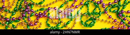 Mardi Gras Konzept. Bunte Perlen auf gelbem Hintergrund. Festliche Karnevalssymbole. Goldene grüne und violette Dekorationen für den Urlaub. Bannerformat, Stockfoto