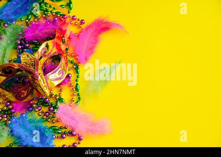 Karnevalsmaske mit Federn auf gelbem Hintergrund. Bunte Perlen in grün, Gold und lila. Symbol „Mardi Gras“ oder „Fat Tuesday“. Speicherplatz kopieren. Stockfoto