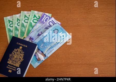 Ansicht des kanadischen Passes mit kanadischem Geld auf braunem Hintergrund. Stockfoto