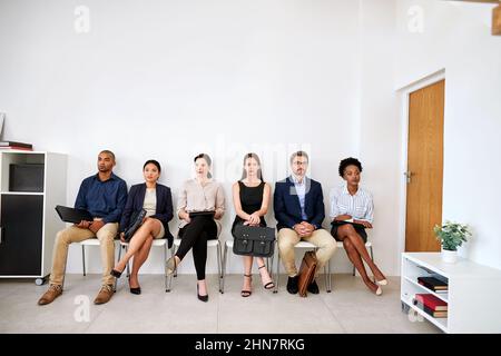 Es ist eine lange Wartezeit, aber es wird sich lohnen. Aufnahme einer Gruppe von Geschäftsleuten, die in der Schlange saßen, während sie darauf warteten, interviewt zu werden. Stockfoto