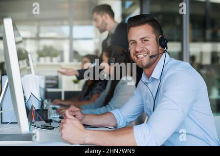 Großartiger Service macht gute Geschäfte. Porträt eines glücklichen und selbstbewussten jungen Mannes, der in einem Callcenter arbeitet. Stockfoto