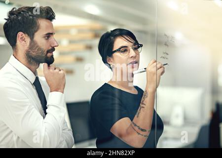 Unter Berücksichtigung aller Optionen. Eine kurze Aufnahme von Geschäftsleuten, die in einem Büro mit Notizen an einer Glaswand Brainstorming durchführen. Stockfoto