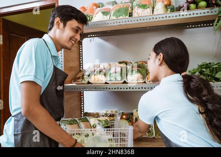Männliche und weibliche Gemüseverkäufer setzen Gemüse auf Vitrine Stockfoto