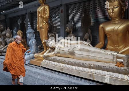 Ein thailändischer buddhistischer Mönch passiert einen schlafenden Buddha eine andere Buddha-Statue, die vor einem Geschäft für buddhistische Gegenstände aufgestellt ist; Bamrung Muang Rd., Bangkok, Thailand Stockfoto