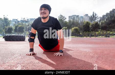Lateinischer Mann, der Cobra Stretch macht und in einem Park trainiert. Konzept von Übungen und Yoga Stockfoto