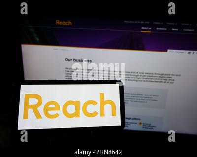 Person, die ein Smartphone mit dem Logo des britischen Verlags Reach plc auf dem Bildschirm vor der Website hält. Konzentrieren Sie sich auf die Telefonanzeige. Stockfoto