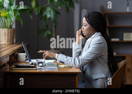 Junge schwarze Geschäftsfrau am Schreibtisch ruft Geschäftspartner an, um über Projektdetails zu sprechen Stockfoto