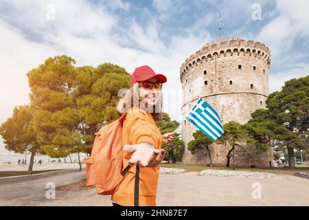 Folge mir, glückliches Studentenmädchen mit griechischer Flagge und Rucksack auf dem Hintergrund des Weißen Turms in Thessaloniki. Konzept der Staatsbürgerschaft oder des Lernens von Gree Stockfoto