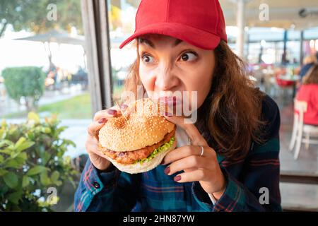 Eine Frau schnüffelt Burger in einem Café mit Ekel auf ihrem Gesicht. Das Konzept der verdorbenen Lebensmittel und Vergiftungen im Catering-Restaurant Stockfoto