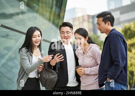 Eine Gruppe junger asiatischer Menschen, die im Freien gemeinsam das Handy angeschaut haben, glücklich und lächelnd Stockfoto