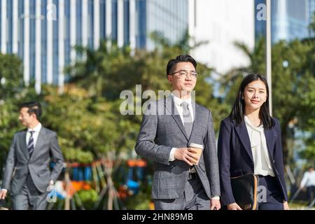 Zwei junge asiatische Geschäftsleute, die in der modernen Stadt draußen auf der Straße spazieren Stockfoto