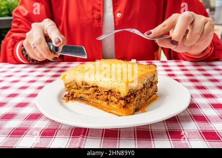 Ein Teller mit authentischem griechischem Moussaka-Auflauf auf einer eleganten Tischdecke in einem Restaurant mit Gabel und Messer. Traditionelle Köstlichkeiten auf dem Balkan. Stockfoto