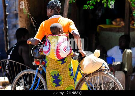 Eine burkinische Frau, die ihr Baby auf dem Rücken auf einem lokalen Markt im Zentrum von Burkina Faso trägt. Stockfoto