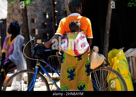 Eine burkinische Frau, die ihr Baby auf dem Rücken auf einem lokalen Markt im Zentrum von Burkina Faso trägt. Stockfoto