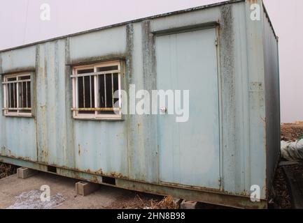 Verwittertes grünes Transportcontainer-Büro in der Nähe der Baustelle Stockfoto