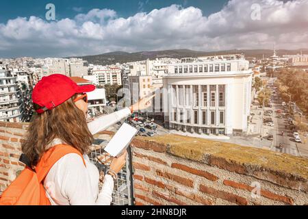 Glückliche Touristenfrau, die auf die nächsten Sehenswürdigkeiten zeigt, während sie auf dem Aussichtspunkt des Weißen Turms steht und das Panorama der Stadt Thessaloniki in Griechenland genießt Stockfoto