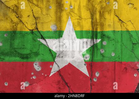 Vollformatfoto einer verwitterten Flagge von Myanmar, gemalt auf einer rissigen Wand mit Einschusslöchern. Myanmar Krise und ethnische Gewalt Konzept. Stockfoto