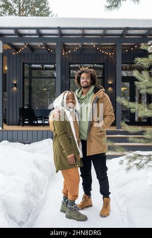 Porträt eines jungen afrikanischen Paares, das am Wintertag im Freien gegen ihr Haus steht und die Kamera anlächelt Stockfoto