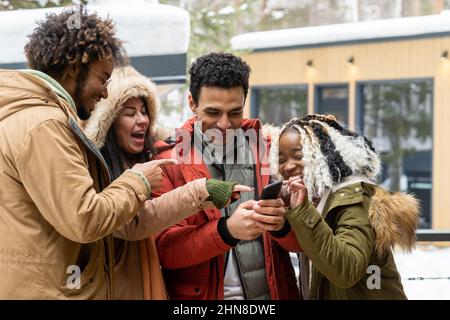 Eine Gruppe von glücklichen Freunden, die sich lustige Videos auf dem Smartphone ansehen und gemeinsam im Freien lachen Stockfoto