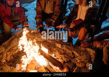 Nahaufnahme von Menschen, die im Winter in der Nähe des Lagerfeuers sitzen und ihre Hände über der Flamme erwärmen Stockfoto