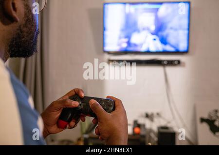 Nahaufnahme eines afrikanischen Mannes, der die Tasten auf der Konsole drückt, während er Videospiele im Zimmer zu Hause spielt Stockfoto