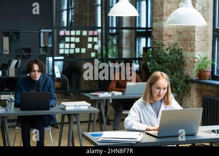 Junge Geschäftsleute, die an ihren Arbeitsplätzen im Büro sitzen und an Computern arbeiten, machen ihre Online-Arbeit Stockfoto