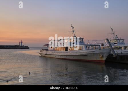 Jalta, Krim, Russland-10.25.2019: Boote auf Jalta Böschung früh am Morgen in rosa Licht, Leuchtturm. Die Hauptstadt der Südküste von Crime Stockfoto