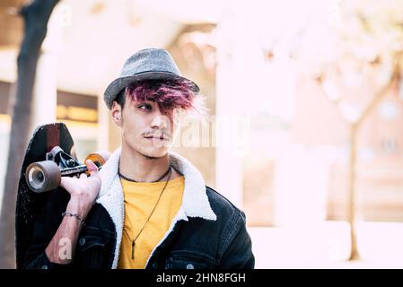 Trendy Teenager junge Porträt halten Skate Board und trägt Hut. Diversity Teenager Menschen mit farbigen violetten Haaren und Schnurrbärte auf seiner Seite ein Stockfoto