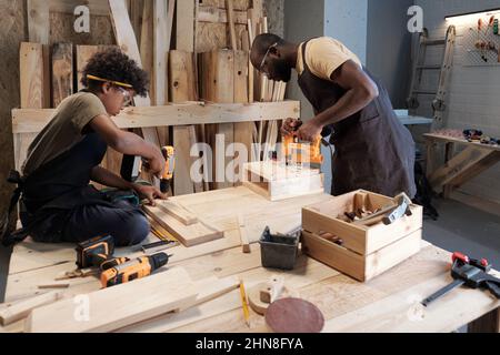 Seitenansicht Porträt von afroamerikanischem Vater und Sohn, die zusammen in der Schreinerei arbeiten Stockfoto